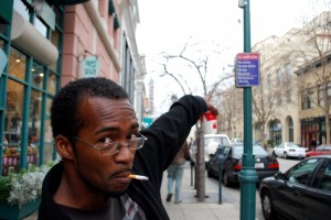 DSC_1027 A man smoking on Pacific Avenue points out the law. The smoking ban, seen on the sign, went into effect on Oct. 20 after a one month grace period. CHP Archives.